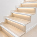 White aluminium LED stair nosing profiles with warm LED glow on cream limestone steps