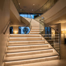 LED tile-in stair nosings lighting the risers of a wide tiled hotel lobby staircase with glass balustrade