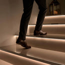 Person climbing dark tiled stairs edge-lit by concealed LED stair nosing lighting