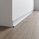 Silver anodised aluminium internal corner trim fitted along the junction where a grey oak-effect LVT floor meets a white wall in a hallway