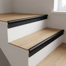 Matt black anodised stair nosing fitted to light oak LVT steps with white risers, the vinyl butting the smooth rounded bead with a shallow ribbed band down the top of the riser