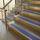 Brass stair nosings with mid blue ribbed inserts on stone steps beside a glass balustrade