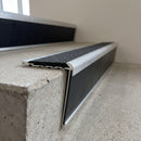 Aluminium 78.5x67mm raked-back carborundum stair nosing in mill finish with black carborundum anti-slip insert, fitted to a concrete step