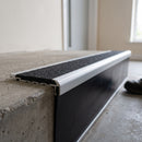 Aluminium 78.5x67mm raked-back carborundum stair nosing in satin finish with black carborundum anti-slip insert, fitted to a concrete step
