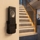 Multi-zone LED remote control on a hallway wall beside a staircase with warm lit tiled steps