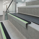 Black and photoluminescent green insert nosings on concrete office stairs beside a glass balustrade