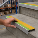 Hand positioning a yellow and green insert stair nosing onto a concrete step edge in a warehouse