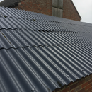 Charcoal grey encapsulating roof paint freshly applied to an asbestos cement roof on a UK outbuilding, sealing and restoring the surface