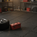 Black interlocking EVA foam floor tiles covering a home workshop floor with a car tyre and toolbox