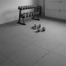 Grey interlocking EVA foam floor tiles covering a home garage gym floor with a dumbbell rack