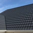 Dark grey weatherproof paint freshly applied to concrete roof tiles on a UK house roof, restoring colour and sealing against rain