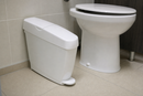 White pedal operated sanitary bin standing beside a toilet in a commercial washroom cubicle