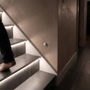 PIR motion sensor in a hallway wall beside a staircase whose LED nosings light as someone climbs
