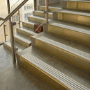 Brass stair nosings with polar grey castellated inserts on stone steps beside a glass balustrade
