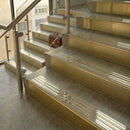Polished brass stair nosings with matching brass ribbed inserts on stone steps beside a glass balustrade