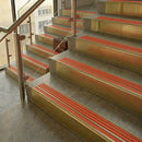 Brass stair nosings with poppy orange ribbed inserts on stone steps beside a glass balustrade