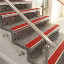 Raked back nosings with poppy red ribbed inserts on mottled stone steps between stainless handrails