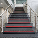 Black PVC hard nose stair nosings with red anti-slip inserts fitted to concrete steps in a commercial stairwell