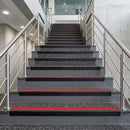 Black PVC hard nose stair nosings with red anti-slip inserts fitted to concrete steps in a commercial stairwell
