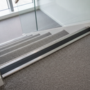 Black anti-slip PVC stair nosing insert strip fitted into an aluminium stair nosing channel on a carpeted staircase