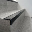 Black flexible PVC stair nosing 40mm x 25mm fitted over the front edge of a grey wood-effect laminate stair tread
