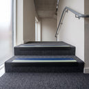 PVC stair nosing 60x32mm with cobalt blue anti-slip insert fitted to grey carpeted steps, green photoluminescent strip along the front edge