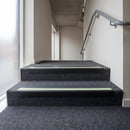 PVC stair nosing 60x32mm with midnight grey anti-slip insert fitted to grey carpeted steps, green photoluminescent strip along the front edge