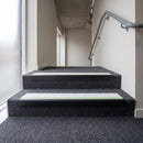 PVC stair nosing 60x32mm with white anti-slip insert fitted to grey carpeted steps, green photoluminescent strip along the front edge
