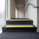 PVC stair nosing 60x32mm with yellow anti-slip insert fitted to grey carpeted steps, green photoluminescent strip along the front edge