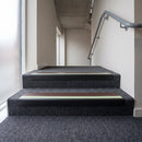 PVC stair nosing 65x36mm with brown anti-slip insert on grey carpeted steps, green photoluminescent strip at the nose
