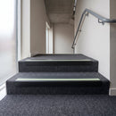 PVC stair nosing 65x36mm with midnight grey anti-slip insert on grey carpeted steps, green photoluminescent strip at the nose