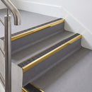 Rake back aluminium stair nosing with a dark charcoal Mor Grip insert in mirrorflect gold finish fitted on an office stair finished in grey lino