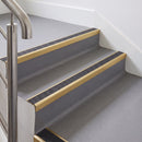 Rake back aluminium stair nosing with a dark charcoal Mor Grip insert in satin gold finish fitted on an office stair finished in grey lino