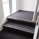 Rake back aluminium stair nosing with a dark charcoal Mor Grip insert in bright polished finish fitted on an office stairwell finished in charcoal contract carpet