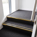 Rake back aluminium stair nosing with a dark charcoal Mor Grip insert in mirrorflect gold finish fitted on an office stairwell finished in charcoal contract carpet