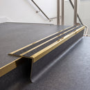 Rake back aluminium stair nosing with twin dark charcoal Mor Grip inserts in mirrorflect gold finish fitted on a college stair finished in dark grey sheet vinyl
