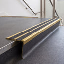 Rake back aluminium stair nosing with twin dark charcoal Mor Grip inserts in satin gold finish fitted on a college stair finished in dark grey sheet vinyl