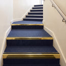 Heavy duty rake back aluminium stair nosing with black insert in mirrorflect gold finish fitted on a stair with navy contract carpet