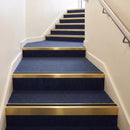 Heavy duty rake back aluminium stair nosing with black insert in satin gold finish fitted on a stair with navy contract carpet