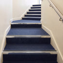 Heavy duty rake back aluminium stair nosing with black insert in bright polished finish fitted on a stair with navy contract carpet