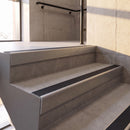Mill Finish rake back DDA aluminium stair nosing 70 x 56mm with Obsidian black High Grip insert, fitted on raked concrete stairs in a commercial stairwell