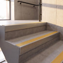 Mill Finish rake back DDA aluminium stair nosing 70 x 56mm with Solar yellow High Grip insert, fitted on raked concrete stairs in a commercial stairwell