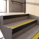 Satin Black rake back DDA aluminium stair nosing 70 x 56mm with Brimstone yellow Exterior Grip insert, fitted on raked concrete stairs in a commercial stairwell