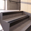 Satin Black rake back DDA aluminium stair nosing 70 x 56mm with Coal black Exterior Grip insert, fitted on raked concrete stairs in a commercial stairwell