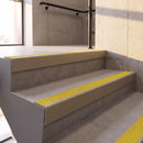 Satin Bronze rake back DDA aluminium stair nosing 70 x 56mm with Brimstone yellow Exterior Grip insert, fitted on raked concrete stairs in a commercial stairwell