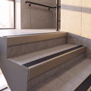 Satin Bronze rake back DDA aluminium stair nosing 70 x 56mm with Obsidian black High Grip insert, fitted on raked concrete stairs in a commercial stairwell