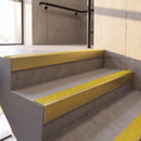 Satin Gold rake back DDA aluminium stair nosing 70 x 56mm with Brimstone yellow Exterior Grip insert, fitted on raked concrete stairs in a commercial stairwell