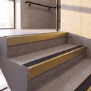 Satin Gold rake back DDA aluminium stair nosing 70 x 56mm with Coal black Exterior Grip insert, fitted on raked concrete stairs in a commercial stairwell