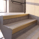 Satin Gold rake back DDA aluminium stair nosing 70 x 56mm with Everest light grey Exterior Grip insert, fitted on raked concrete stairs in a commercial stairwell