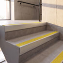 Satin Silver rake back DDA aluminium stair nosing 70 x 56mm with Brimstone yellow Exterior Grip insert, fitted on raked concrete stairs in a commercial stairwell